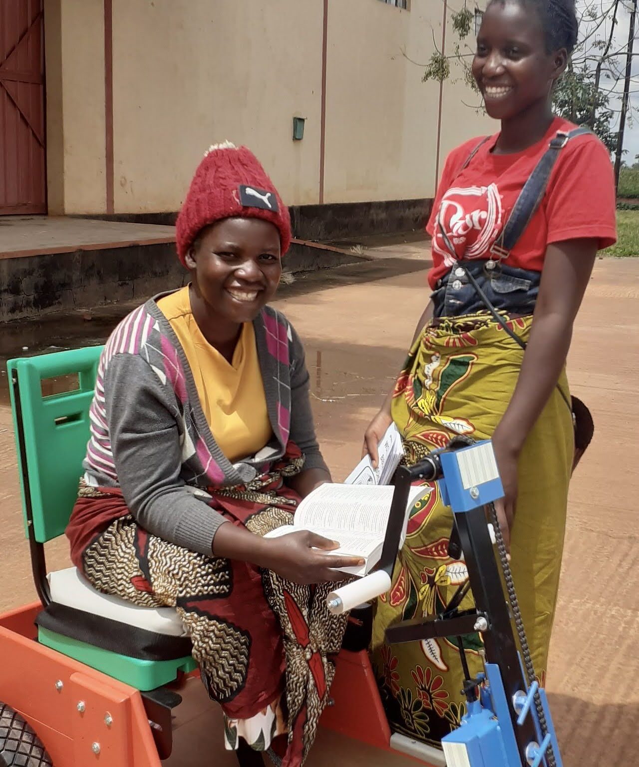 Two women together one seated in a mobility cart and the other standing next to her both smiling